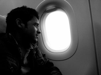 Young man looking through window in airplane