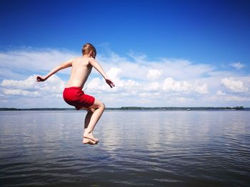 Shirtless boy diving in sea against blue sky during sunny day