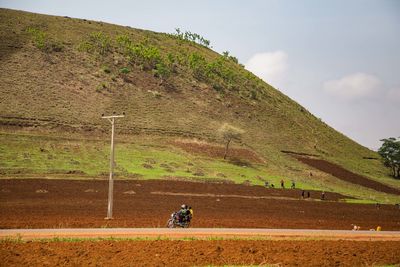 People riding motorcycle on road amidst field against sky