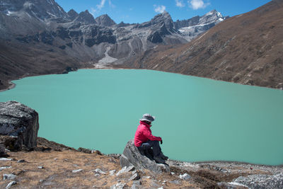 Side view of mid adult woman sitting by lake on rock against mountain during sunny day