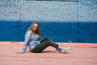 Full length of young woman sitting on footpath