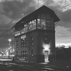 Illuminated street by building against sky at night