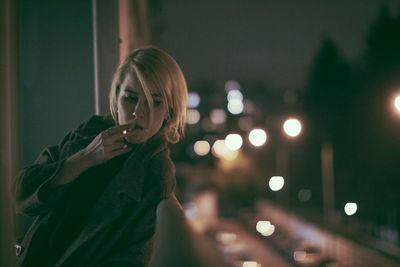 Portrait of woman standing by illuminated light at night