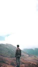 Rear view of man standing on mountain against sky