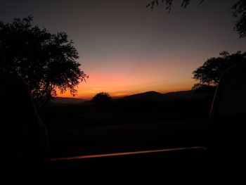 Silhouette trees by road against sky during sunset