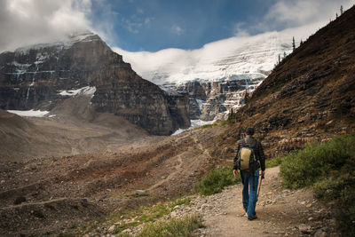 Rear view of man walking on mountains against sky