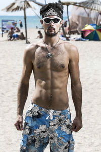 Portrait of shirtless man wearing sunglasses while standing at beach