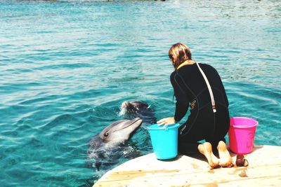 Rear view of caretaker feeding dolphins in pond at aquarium