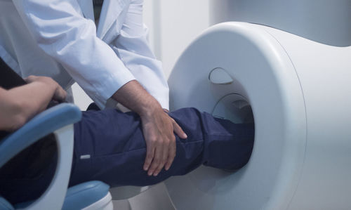 Midsection of doctor putting patient leg in cat scan machine in hospital