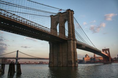 Low angle view of brooklyn bridge over river during sunset