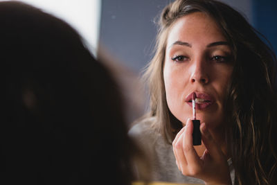 Concentrated charming female with smooth skin applying gloss lipstick while preparing for event