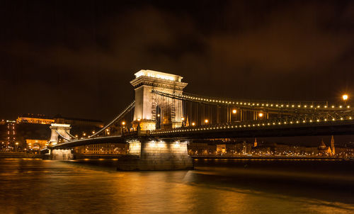 Illuminated bridge over river against sky at night