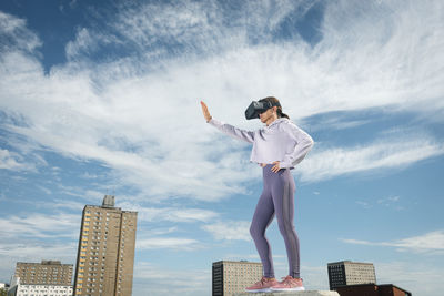 Woman outside wearing virtual reality headset with her arm outstretched, urban backdrop.