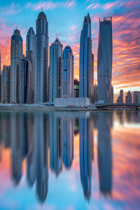Reflection of buildings in city against sky during sunset