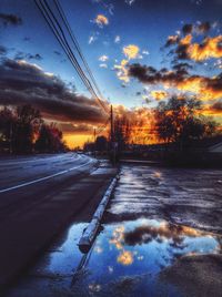 Surface level of road on snow covered landscape against orange sky