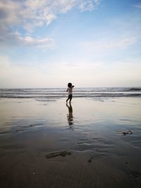 Baby girl playing at beach against sky