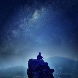 Silhouette man sitting on cliff against star field at night