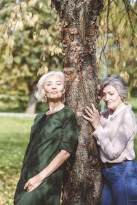 Happy young woman standing by tree trunk