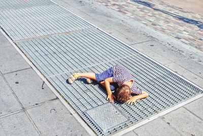 High angle view of boy looking in gutter through metal grate on footpath