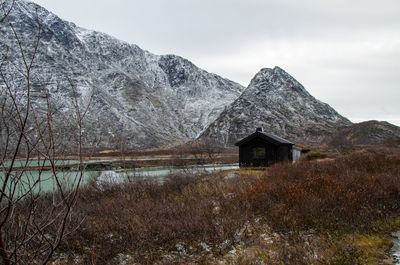 A cozy wooden cabin on the lake shore against snowcapped mountains