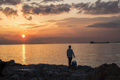 Rear view of man fishing at sea during sunset