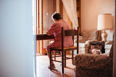 Back view of a senior woman with alzheimer's mental health issues painting on a notebook inside her home