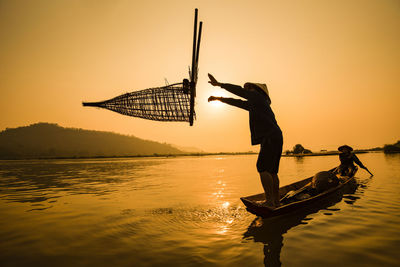 Man casting in lake against clear sky during sunset