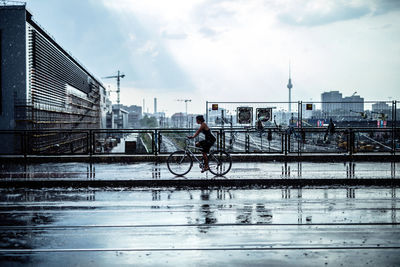 Man riding bicycle on city against sky