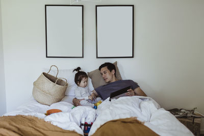 Father with male toddler holding digital tablet in bedroom at home