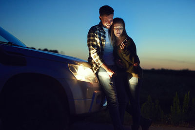 Young man standing by car against sky