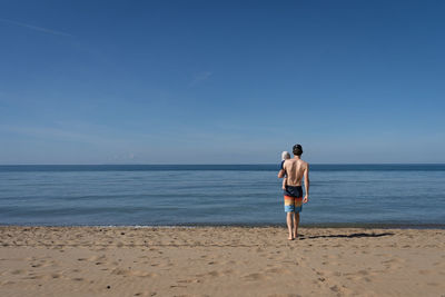 Rear view of woman standing at beach against sky