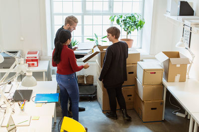 High angle view of business colleagues discussing over documents by cardboard boxes at office