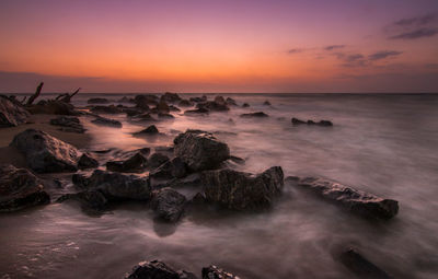 Rocks on shore against sky during sunrise