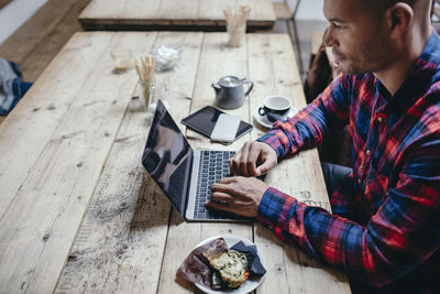 Side view of mid adult man using laptop at table in coffee shop