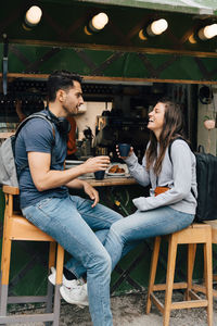 Full length of smiling friends holding coffee cups while sitting by concession stand in city