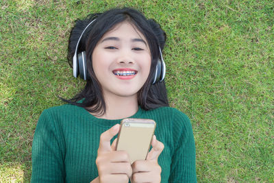 Portrait of smiling young woman using phone lying grassy on field