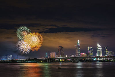 Firework display over illuminated buildings against sky at night