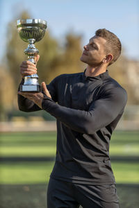 Side view of man holding trophy against sky