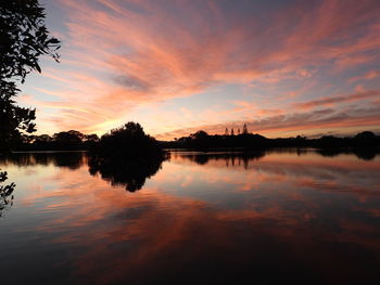 Silhouette trees by lake against sky during sunset