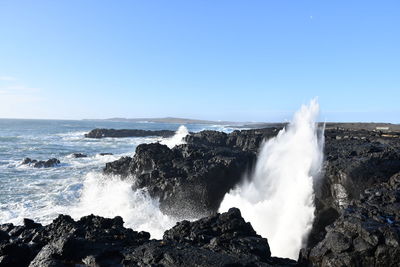 Sea waves splashing on rocks against clear sky