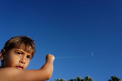 Portrait of boy holding kite against clear blue sky