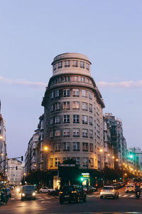 Cars on road by illuminated buildings against sky in city at night