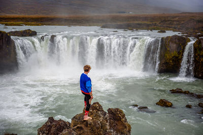 Man standing on rock looking at waterfall