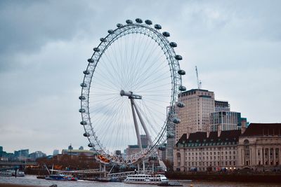 Ferris wheel in city against cloudy sky