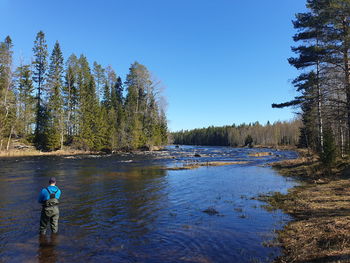 Rear view of man standing by lake against clear blue sky