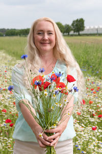 Beautiful middle-aged blonde woman stands among a flowering field of poppies