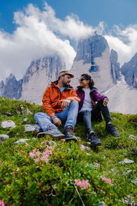 Rear view of people sitting on mountain against sky