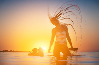 Silhouette of a slender young female athlete kite surfer swims at sunset in the sea next to her kite