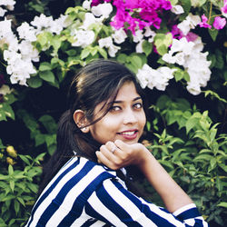 Portrait of smiling young woman against plants looking at camera