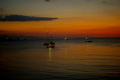 Boats sailing in sea at sunset